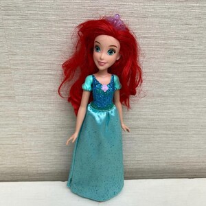 Op de afbeelding: Pop van een personage met felrood haar, gekleed in een turquoise jurk met een sprankelend lijfje en een paarse bloemaccent. De pop heeft blauwe ogen en een tiara. De pop is een populair personage uit een animatiefilm voor kinderen.