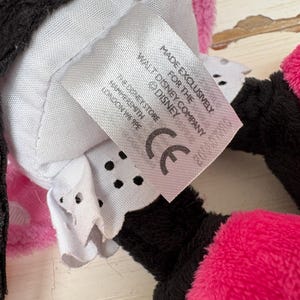 May include: Close-up of a plush toy with pink, black, and white elements. A tag reads "MADE EXCLUSIVELY FOR THE DISNEY COMPANY" and "THE DISNEY STORE HAMMERSMITH LONDON W6 9PE". The toy has a CE mark.