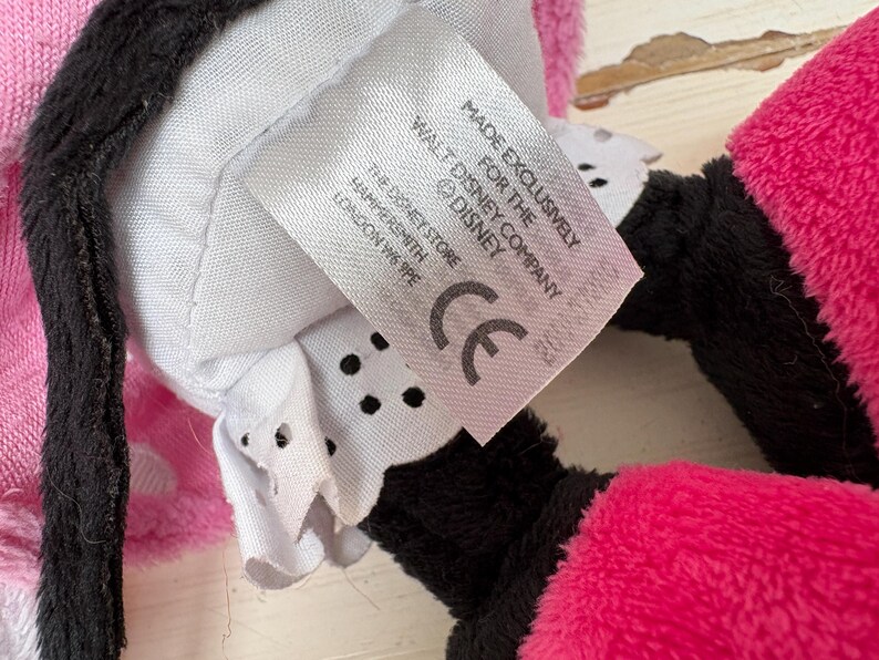 May include: Close-up of a plush toy with pink, black, and white elements. A tag reads "MADE EXCLUSIVELY FOR THE DISNEY COMPANY" and "THE DISNEY STORE HAMMERSMITH LONDON W6 9PE". The toy has a CE mark.