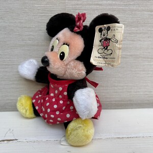K&ouml;nnte beinhalten: Ein Vintage-Minnie-Mouse-Pl&uuml;schtier. Das Pl&uuml;schtier hat ein rotes Kleid mit wei&szlig;en Punkten, gelbe Schuhe und eine rote Schleife. Das Spielzeug hat ein Etikett mit einer Mickey-Mouse-Illustration und dem Text "MINNIE MOUSE".