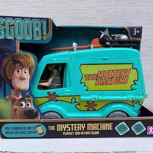 May include: A teal and yellow Mystery Machine playset and action figure, packaged in a box with Scooby-Doo characters. The van features the text "THE MYSTERY MACHINE". The box includes the text "SCOOBY" and "PLAYSET AND ACTION FIGURE".