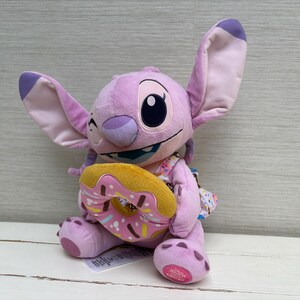 Puede incluir: Un peluche de Angel de Lilo & Stitch, en tonos rosa y morado. El juguete sostiene una rosquilla con glaseado rosa y chispas. El peluche tiene orejas grandes y una expresi&oacute;n traviesa.
