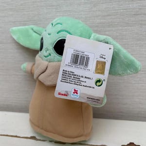 Peut inclure: Poup&eacute;e en peluche Grogu, &eacute;galement connu sous le nom de The Child, de la s&eacute;rie Star Wars. La poup&eacute;e est vert clair avec de grandes oreilles, des yeux noirs et une robe beige. Une &eacute;tiquette de produit est attach&eacute;e. La poup&eacute;e mesure environ 18 cm de haut.