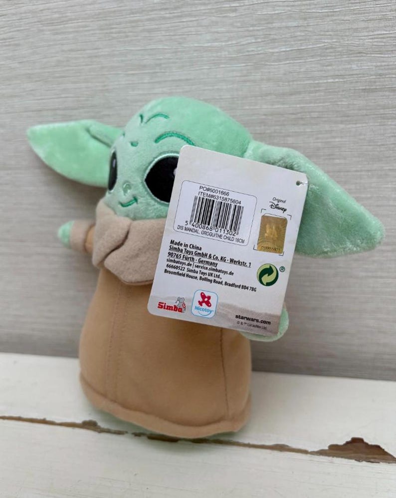 Peut inclure: Poup&eacute;e en peluche Grogu, &eacute;galement connu sous le nom de The Child, de la s&eacute;rie Star Wars. La poup&eacute;e est vert clair avec de grandes oreilles, des yeux noirs et une robe beige. Une &eacute;tiquette de produit est attach&eacute;e. La poup&eacute;e mesure environ 18 cm de haut.