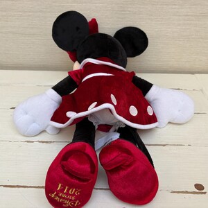 May include: A plush Minnie Mouse doll, with black ears, a red bow, and a red dress with white polka dots. The doll has white gloves and red shoes. The Disney Store 2014 logo is visible on the shoe.
