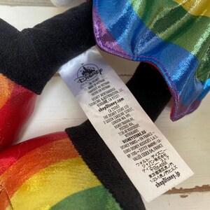 May include: A plush toy with rainbow-coloured accents and a black base. The toy has a tag with the Disney logo and text. The rainbow colours include red, orange, yellow, green, blue, and purple. The toy is made of a shiny material.