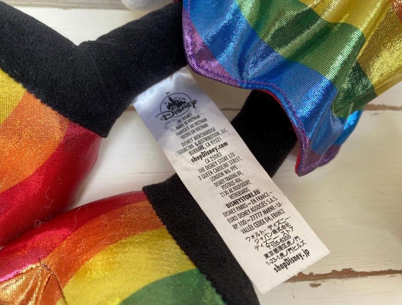May include: A plush toy with rainbow-coloured accents and a black base. The toy has a tag with the Disney logo and text. The rainbow colours include red, orange, yellow, green, blue, and purple. The toy is made of a shiny material.