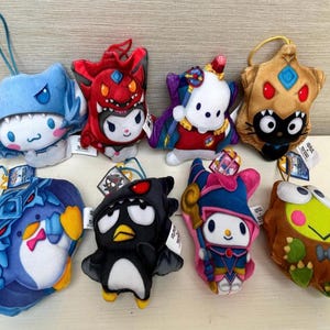 Könnte beinhalten: Eine Sammlung von acht Plüschfiguren in verschiedenen Farben. Die Spielzeuge umfassen einen blauen Hai, einen roten Teufel, eine weiße Figur mit lila Umhang, ein sternförmiges Wesen in Beige, einen blauen Pinguin, einen schwarzen Pinguin, einen rosa Zauberer und einen grünen Frosch.