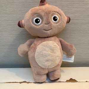 Może przedstawiać: Pluszowa zabawka przedstawiająca postać z serialu dla dzieci, In the Night Garden. Miękka zabawka jest jasnobrązowa z dużymi białymi oczami, uśmiechniętą twarzą oraz małymi ramionami i nogami.