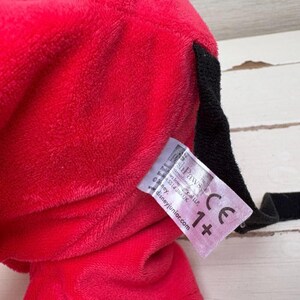 May include: Close-up of a plush red toy with a black accent and a tag. The tag includes the text "shPawS" and "Disneyjunior.com" along with a "CE" mark and "1+" symbol.