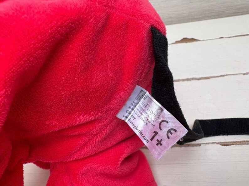May include: Close-up of a plush red toy with a black accent and a tag. The tag includes the text "shPawS" and "Disneyjunior.com" along with a "CE" mark and "1+" symbol.