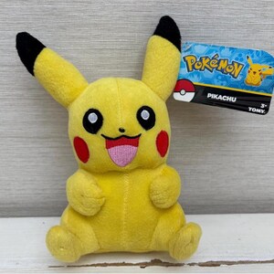 May include: A yellow Pikachu plush toy with black-tipped ears, red cheeks, and a pink tongue. The plush has a tag that reads "Pokémon" and "Pikachu". The toy is made of soft material and is suitable for children aged 3 and up.