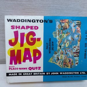 Pode incluir: Uma caixa de quebra-cabeça vintage Waddington's Shaped Jig-Map. A caixa é branca e azul, com as palavras "SHAPED JIG-MAP" em letras grandes e coloridas. O tamanho do quebra-cabeça é de 40,6 x 58,4 cm. A caixa apresenta um mapa do sul da Europa.