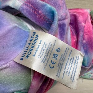 May include: A Build-A-Bear Workshop plush toy with a colorful tie-dye pattern in shades of pink, purple, blue, and green. The toy has a tag with the brand's logo and product information.
