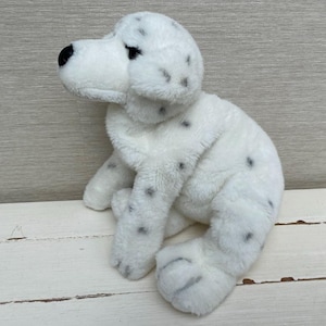 Könnte beinhalten: Ein Stofftier in Form eines sitzenden Dalmatiner-Hundes. Das Spielzeug ist weiß mit schwarzen Flecken, schwarzen Augen und einer schwarzen Nase. Das Plüschtier besteht aus einem weichen, flauschigen Material.