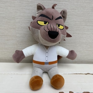May include: A plush toy of a cartoon character with a wolf-like appearance. The toy has a brown and gray head with yellow eyes, a white shirt, gray pants, and brown shoes. It has an orange belt and is sitting upright.