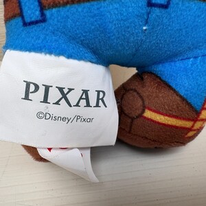 May include: Close-up of a plush toy's leg and tag. The toy has blue pants with brown accents and a brown boot. The tag reads "PIXAR" and "&copy;Disney/Pixar".