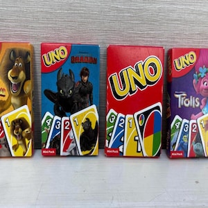 May include: Four mini packs of UNO card games featuring different themes. The packs include "Madagascar", "How to Train Your Dragon", a classic red UNO pack, and "Trolls". Each pack displays the UNO logo and card images.