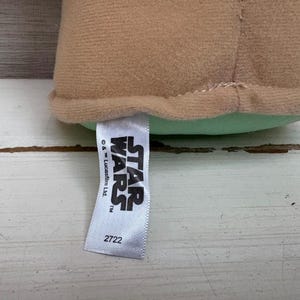 Peut inclure: Un jouet en peluche beige avec une base vert clair. Une &eacute;tiquette blanche avec le logo Star Wars et le num&eacute;ro 2722 est attach&eacute;e au jouet.