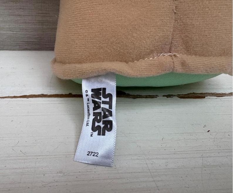 Peut inclure: Un jouet en peluche beige avec une base vert clair. Une &eacute;tiquette blanche avec le logo Star Wars et le num&eacute;ro 2722 est attach&eacute;e au jouet.
