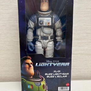 May include: Buzz Lightyear action figure in a box. The figure is wearing a white and grey spacesuit with blue gloves. The box features the Disney Pixar Lightyear logo and the text "XL-01 Buzz Lightyear".