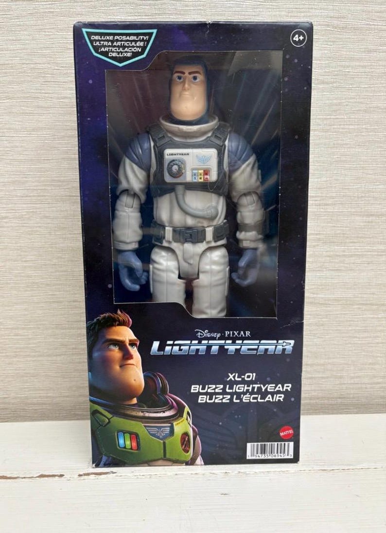 May include: Buzz Lightyear action figure in a box. The figure is wearing a white and grey spacesuit with blue gloves. The box features the Disney Pixar Lightyear logo and the text "XL-01 Buzz Lightyear".