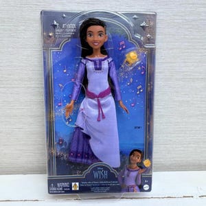 May include: A doll in a clear plastic package. The doll has dark hair and is wearing a purple dress with a pink belt. The packaging has the word "WISH" and musical notes printed on it.