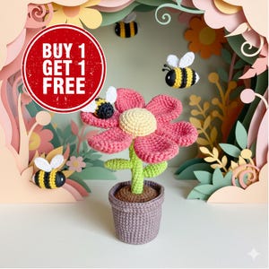 May include: A crocheted flower with pink petals, a yellow center, and a green stem sits in a gray pot. Three crocheted bees fly around the flower. The image includes a red circle with the text "BUY 1 GET 1 FREE".