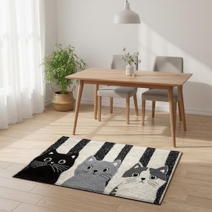 Può includere: Un tappeto rettangolare con tre facce di gatto in bianco, grigio e nero su uno sfondo a strisce. Il tappeto è posizionato su un pavimento in legno, con un tavolo e sedie in legno sullo sfondo. Il design del tappeto aggiunge un tocco giocoso alla stanza.