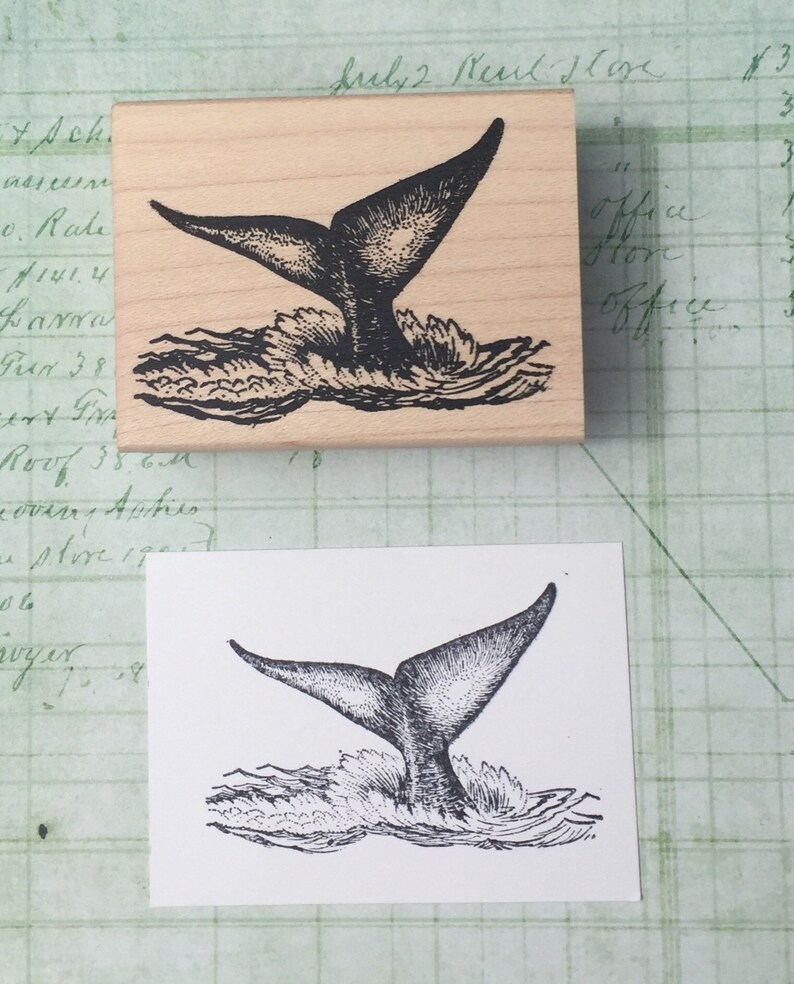 May include: A black and white illustration of a whale tail splashing in the water. The image is printed on a wooden block.
