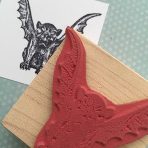 May include: A red rubber stamp with a detailed image of a bat with its wings spread wide. The bat has a menacing expression with sharp teeth and a textured surface.