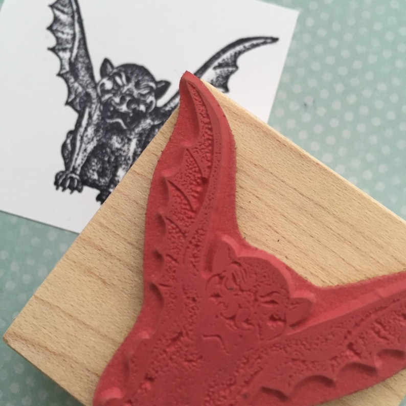 May include: A red rubber stamp with a detailed image of a bat with its wings spread wide. The bat has a menacing expression with sharp teeth and a textured surface.