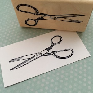 May include: A black and white illustration of a pair of scissors on a white card.