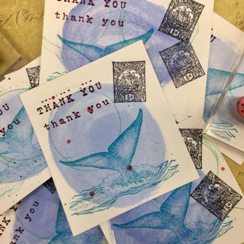 May include: A stack of thank you cards with a blue whale tail design and a vintage stamp. The cards have the text "Thank You" repeated multiple times.