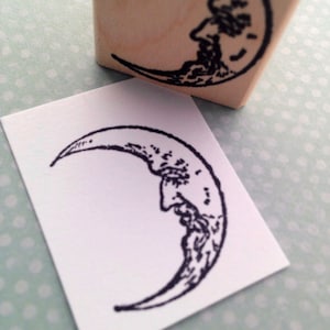 May include: A black and white line drawing of a crescent moon with a face on it. The moon is in the shape of a crescent and the face is detailed with eyes, nose, and mouth.