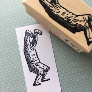 Pode incluir: Ilustração em preto e branco de uma pessoa em uma pose de yoga. A pessoa está em pé em uma perna com a outra perna dobrada atrás dela. Seus braços estão levantados acima de sua cabeça.