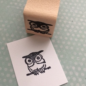 May include: A wooden stamp with a black and white illustration of an owl perched on a branch. The stamp is used to create a similar image on paper.