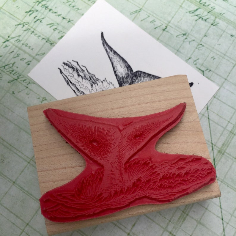 May include: A red rubber stamp with a detailed design of a bird with its wings spread. The stamp is mounted on a wooden block.