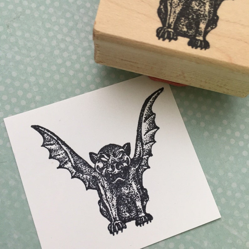 May include: A black and white rubber stamp with a gargoyle design. The gargoyle has wings and a menacing expression.