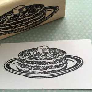 May include: A black and white illustration of a stack of pancakes with a pat of butter on top, on a white plate.