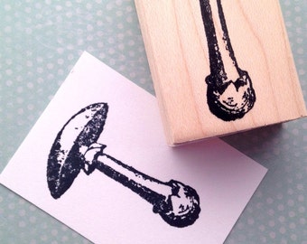 May include: A black and white rubber stamp of a mushroom with a rounded cap and a thick stem. The stamp is mounted on a wooden block.
