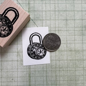 May include: A black and white illustration of a combination padlock with the numbers 36 to 44 visible. The padlock is on a white background next to a US quarter.