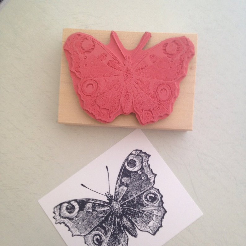 Puede incluir: Un sello de madera con un dise&ntilde;o de mariposa roja. La mariposa tiene un patr&oacute;n detallado de c&iacute;rculos y espirales.