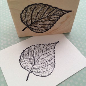 May include: A black and white rubber stamp with a detailed stippled design of a leaf. The stamp is mounted on a wooden block.