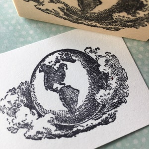Op de afbeelding: Een zwart-witte illustratie van de aarde, omringd door wolken. De aarde is getekend in een vintage stijl met gedetailleerde lijnen.