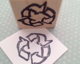 Könnte beinhalten: Ein Stempel aus Holz mit einem schwarzen Recycling-Symbol. Der Stempel wird verwendet, um ein schwarzes Recycling-Symbol auf einer weißen Oberfläche zu erstellen.