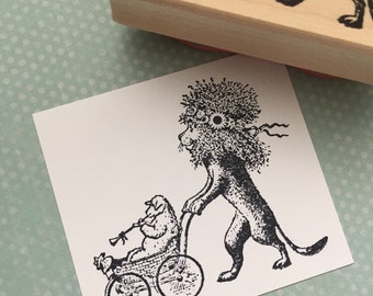 May include: A black and white rubber stamp featuring a lion pushing a baby carriage with a dog playing a wind instrument. The stamp is on a white card with a light green polka dot background. The stamp is made of wood.