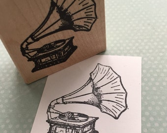 May include: A vintage-style rubber stamp with a black and white illustration of a gramophone with a large horn.