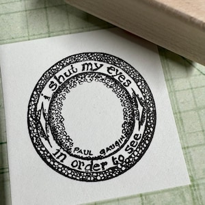 May include: A black and white circular stamp with the text "I shut my eyes in order to see" and the name "Paul Gauguin" inside the circle.