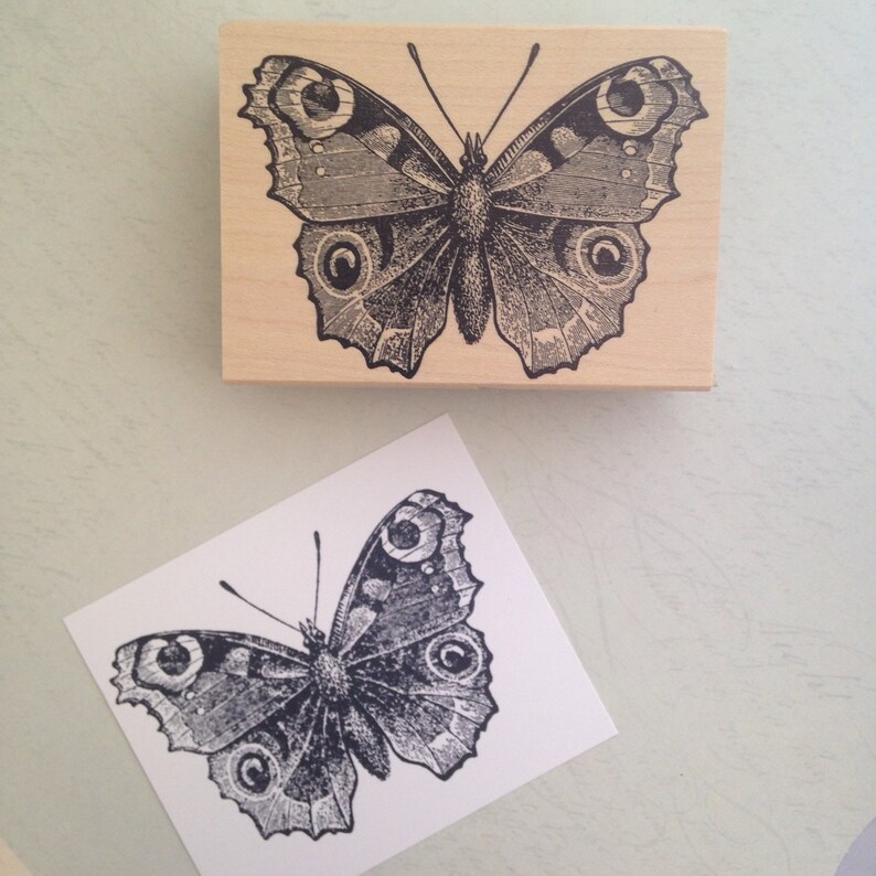 Puede incluir: Un sello de goma de madera con una ilustraci&oacute;n en blanco y negro de una mariposa. La mariposa tiene detalles intrincados y un patr&oacute;n detallado en sus alas.